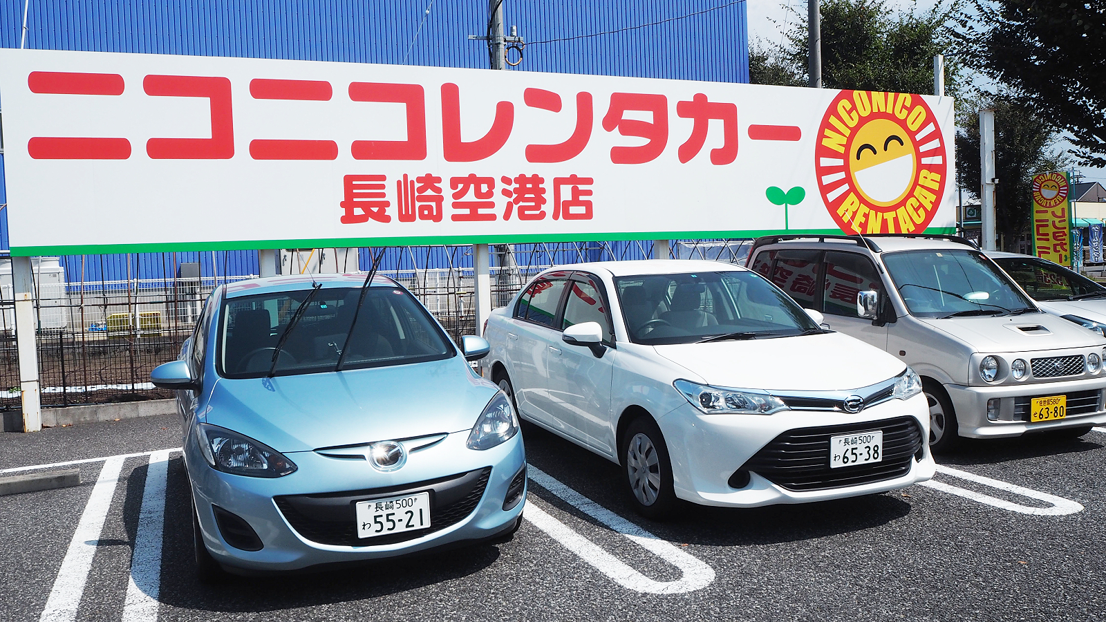Blue, White, and Red Japanese cars under a NICONICO Rent a Car billboard.
