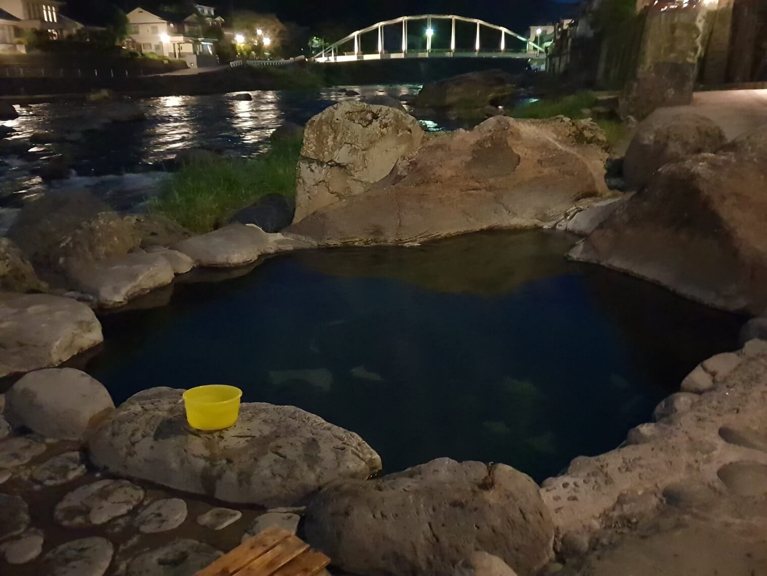 A hot spring pool at night, with a yellow bucket sitting on a rock.