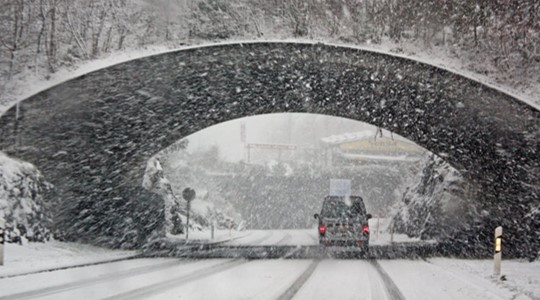 Car driving through tunnel with snow falling in the background.