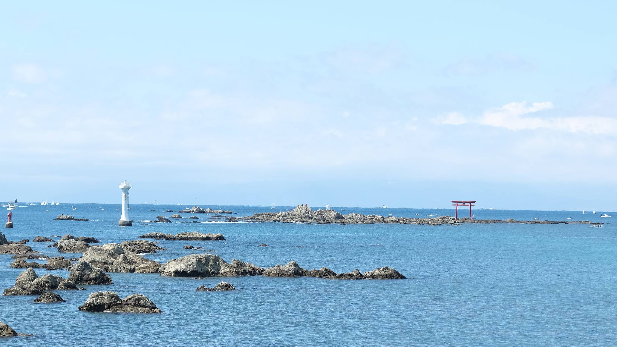 Rocks in the ocean with a red tori gate on one of them.