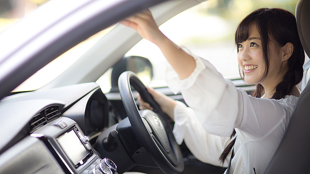 Woman smiling in a Japanese car and adjusting rearview mirror.