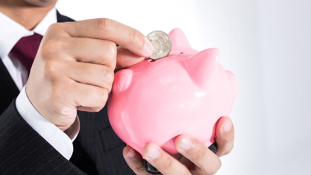 Man in a suit putting a coin in a pink piggy bank.